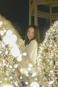 Portrait of woman standing by illuminated lights at night