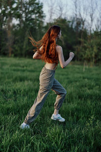 Full length of woman with arms outstretched standing on grassy field