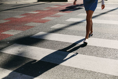 Low section of woman crossing road in city