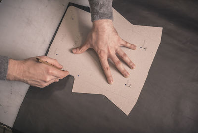 Cropped hands of shoemaker cutting leather with awl on workbench at workshop