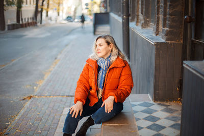 Portrait of woman sitting on footpath in city