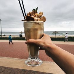 Cropped image of person holding sea against sky