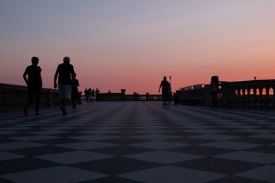 Silhouette people walking on shore against sky during sunset