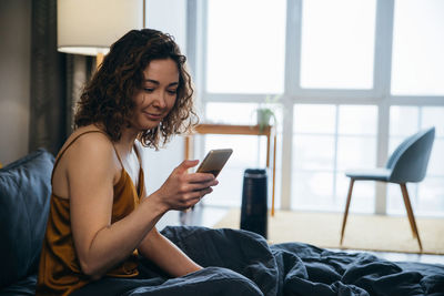 Pretty young woman in her bed with mobile phone