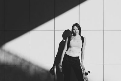 Portrait of woman with skateboard standing against wall