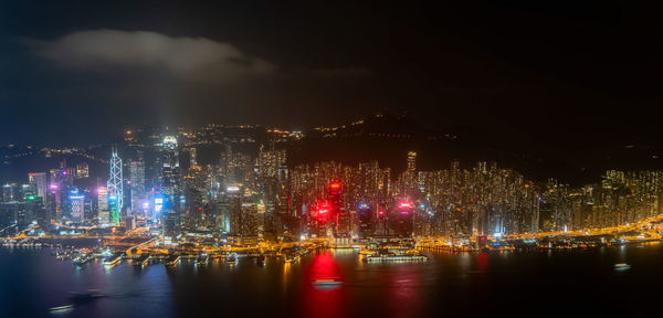 Illuminated buildings by river against sky at night