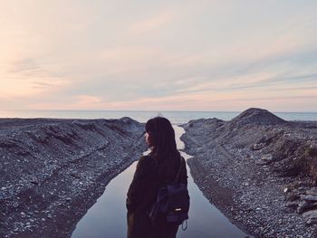 Woman standing by sea against sky during sunset