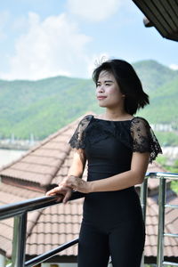 Young woman looking away while standing by railing against clear sky in balcony