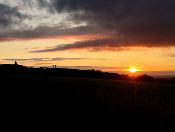 Scenic view of silhouette field against orange sky