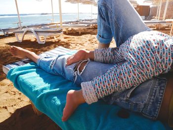 Low section of baby lying on parent on chair at beach