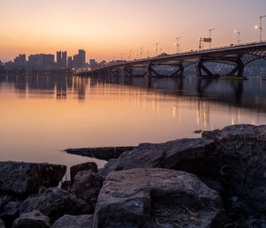 Bridge over river in city against sky during sunset