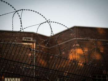 Close-up of barbed wire fence against brick building and sky