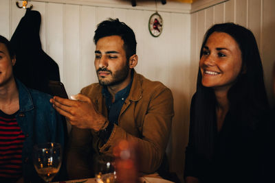Young man using smart phone while sitting amidst female friends in restaurant during dinner party