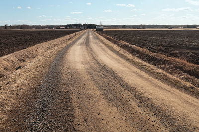 Road passing through agricultural field against sky