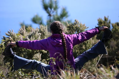 Rear view of woman stretching legs on field against trees