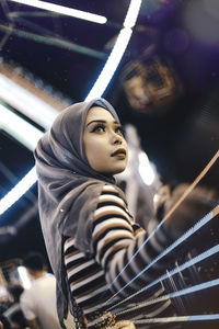 Low angle view of young woman standing in amusement park at night