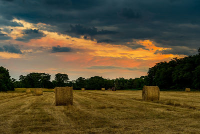 Hay bales on field against sky during sunset