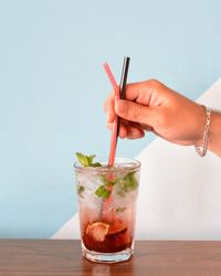 Close-up of man hand holding drinking straws in cold drink against wall