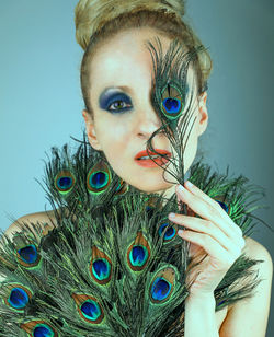 Portrait of woman holding peacock feathers on blue background
