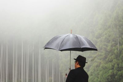 Rear view of man with umbrella on rainy day