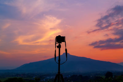 Silhouette camera against mountains during sunset