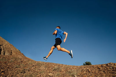 Low angle view of man jumping against clear blue sky