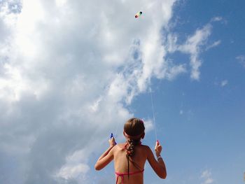 Rear view of girl flying kite against sky