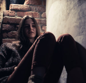 Portrait of young woman sitting against wall