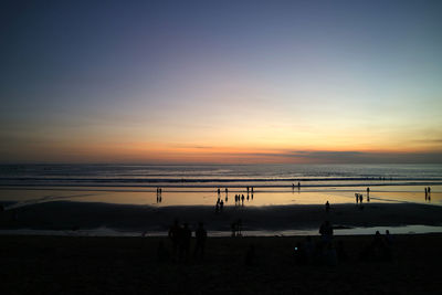 Silhouette people playing on beach against sky during sunset