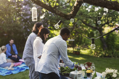 Friends preparing food at table in yard during summer party