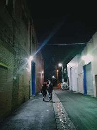 Rear view of people walking on footpath amidst buildings in city