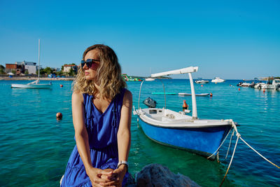 Portrait of young woman sitting on boat in sea against clear blue sky