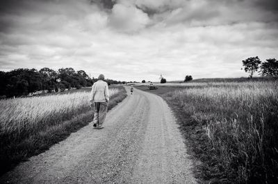 Road passing through field against cloudy sky