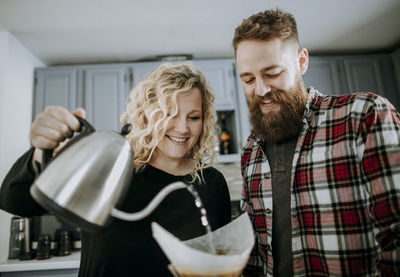 Smiling young couple makes pour over coffee in their kitchen