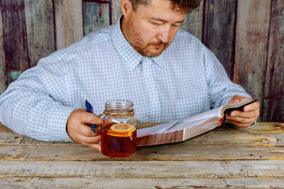 Man reading book while having drink at table