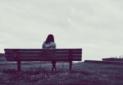 Woman sitting on bench against sky
