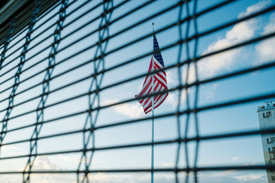 Low angle view of american flag seen through window against sky