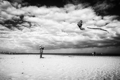 Side view of boy flying kite while standing on beach