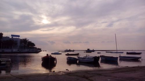 Sailboats moored in sea against sky at sunset