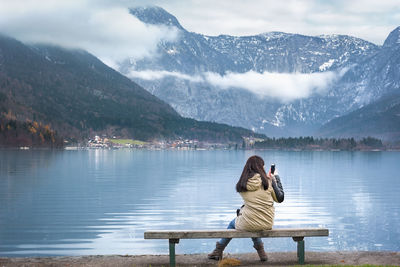 Rear view of woman photographing lake against mountain range