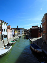 Boats moored in canal amidst buildings in city against sky