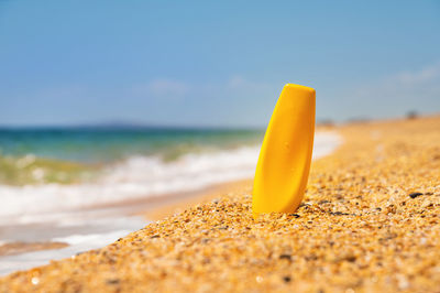 Sandy beach and sea, yellow bottle with suntan oil or sunscreen for burns