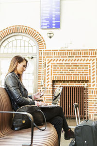 Businesswoman using smart phone while sitting at waiting area in railway station