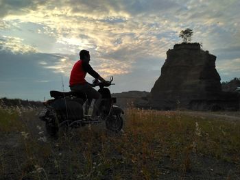 Man riding motorcycle on field against sky during sunset