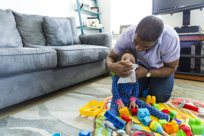 Father wiping daughter's mouth with napkin while kneeling on carpet at home