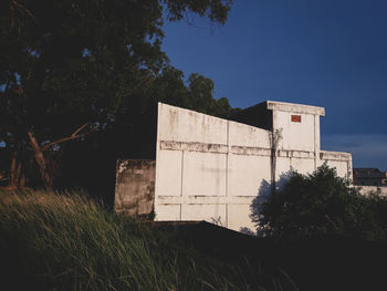 Abandoned building by trees against clear blue sky