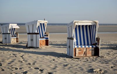 Hooded chairs on beach against sky