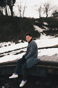 Portrait of man sitting on pier by snow during winter