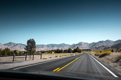 Road leading towards mountains against clear sky