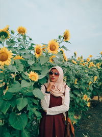 Portrait of young woman standing against sunflower